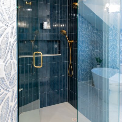 en-suite addition glass door shower with blue tile walls and gold fixtures